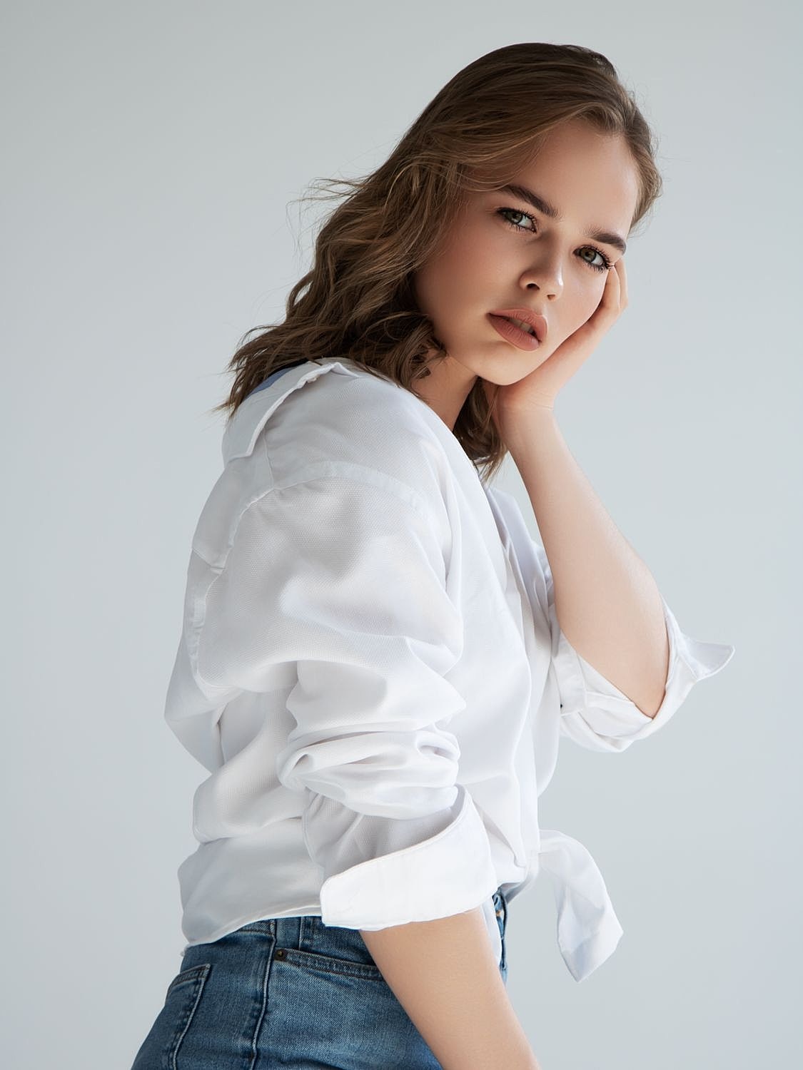 Model in white shirt posing thoughtfully against backdrop