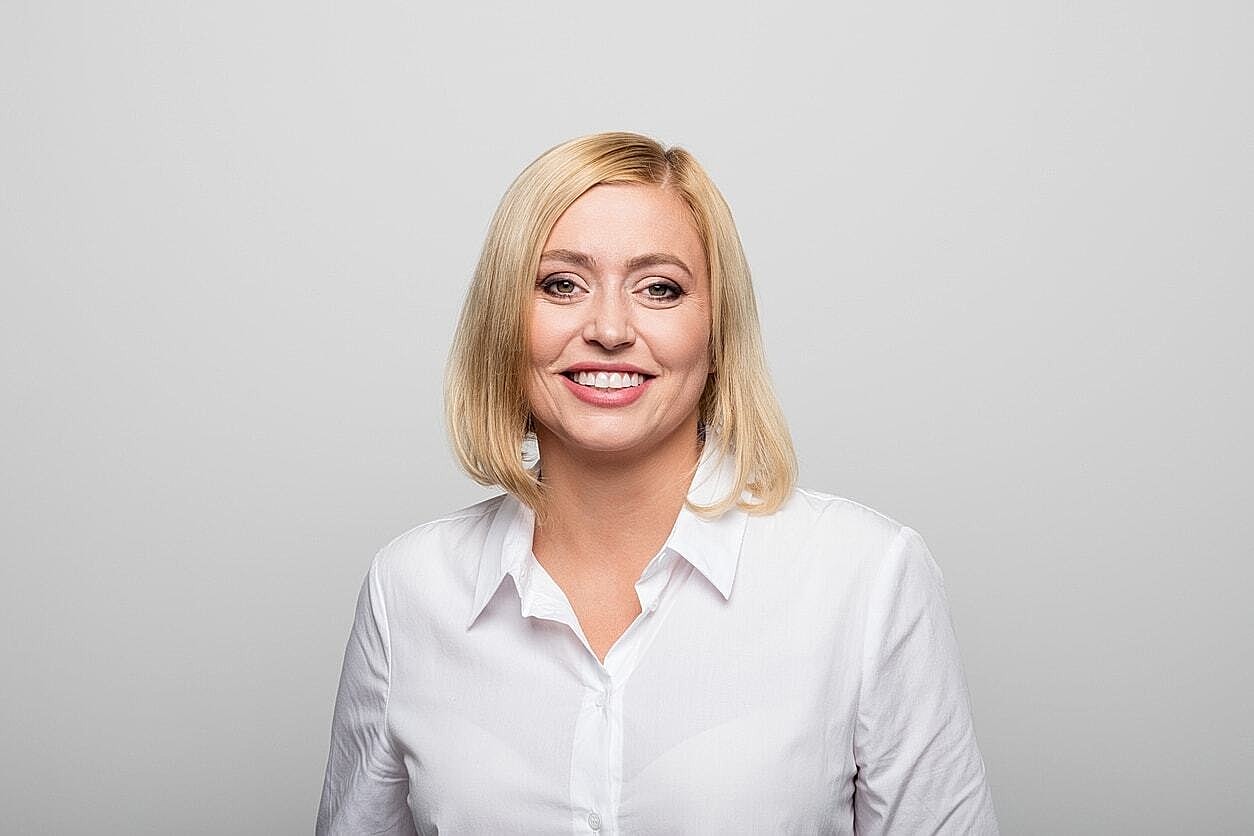 Smiling woman in white shirt against gray background.